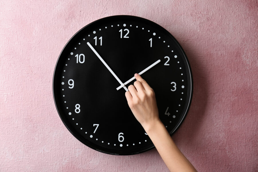 A woman's hand changing time on a clock for daylight savings.