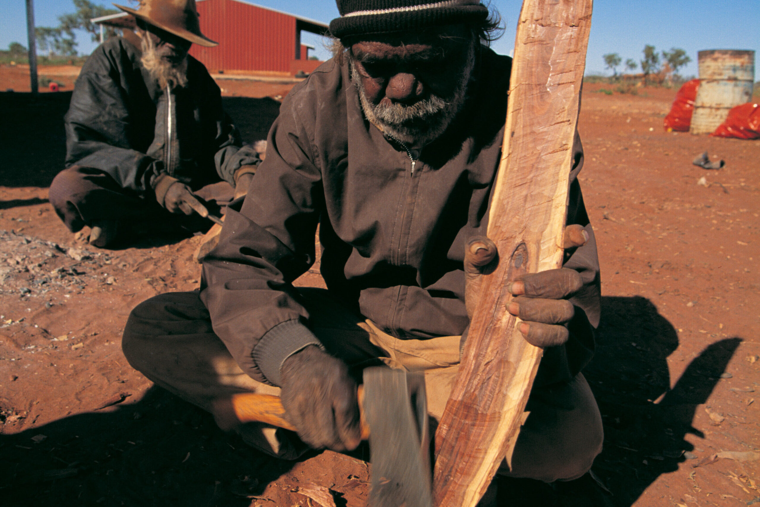 An aboriginal man carving a boomerang from mulga wood