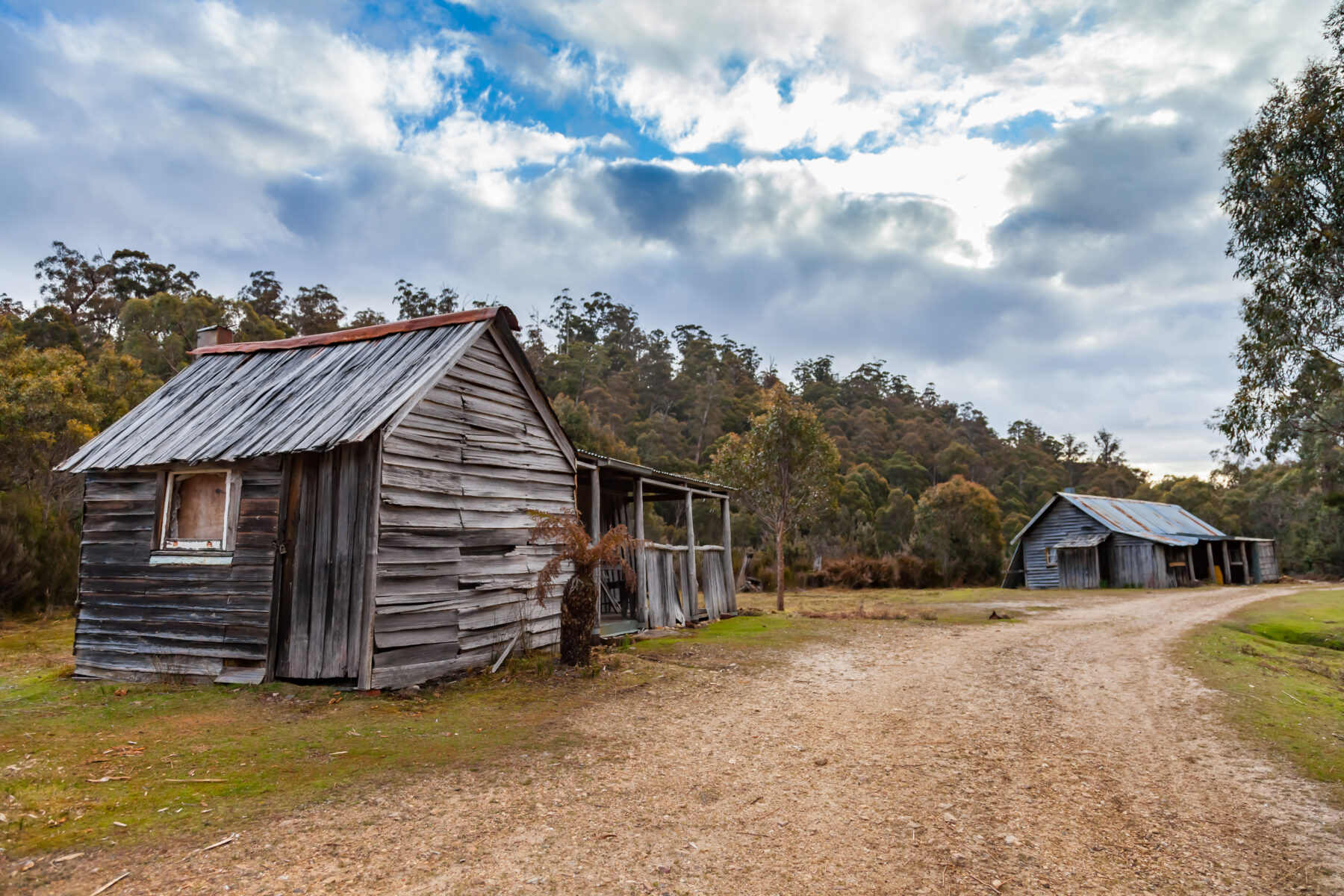 Two historic huts along a dirt path in Adamsfield, Tasmania.