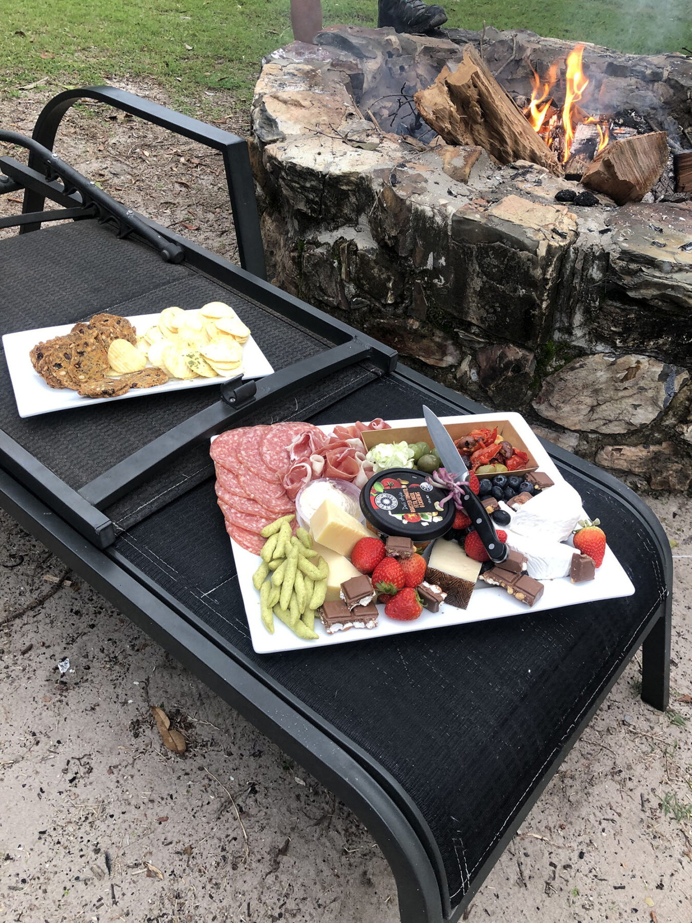 A cheese and fruit platter in front of a campfire