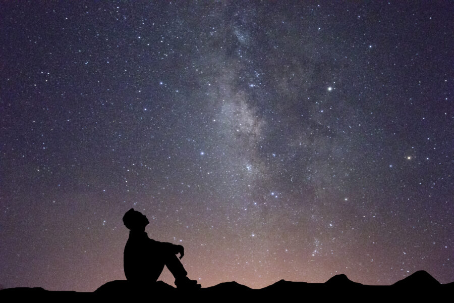 Silhouette of a man sitting and looking up at the Milky Way