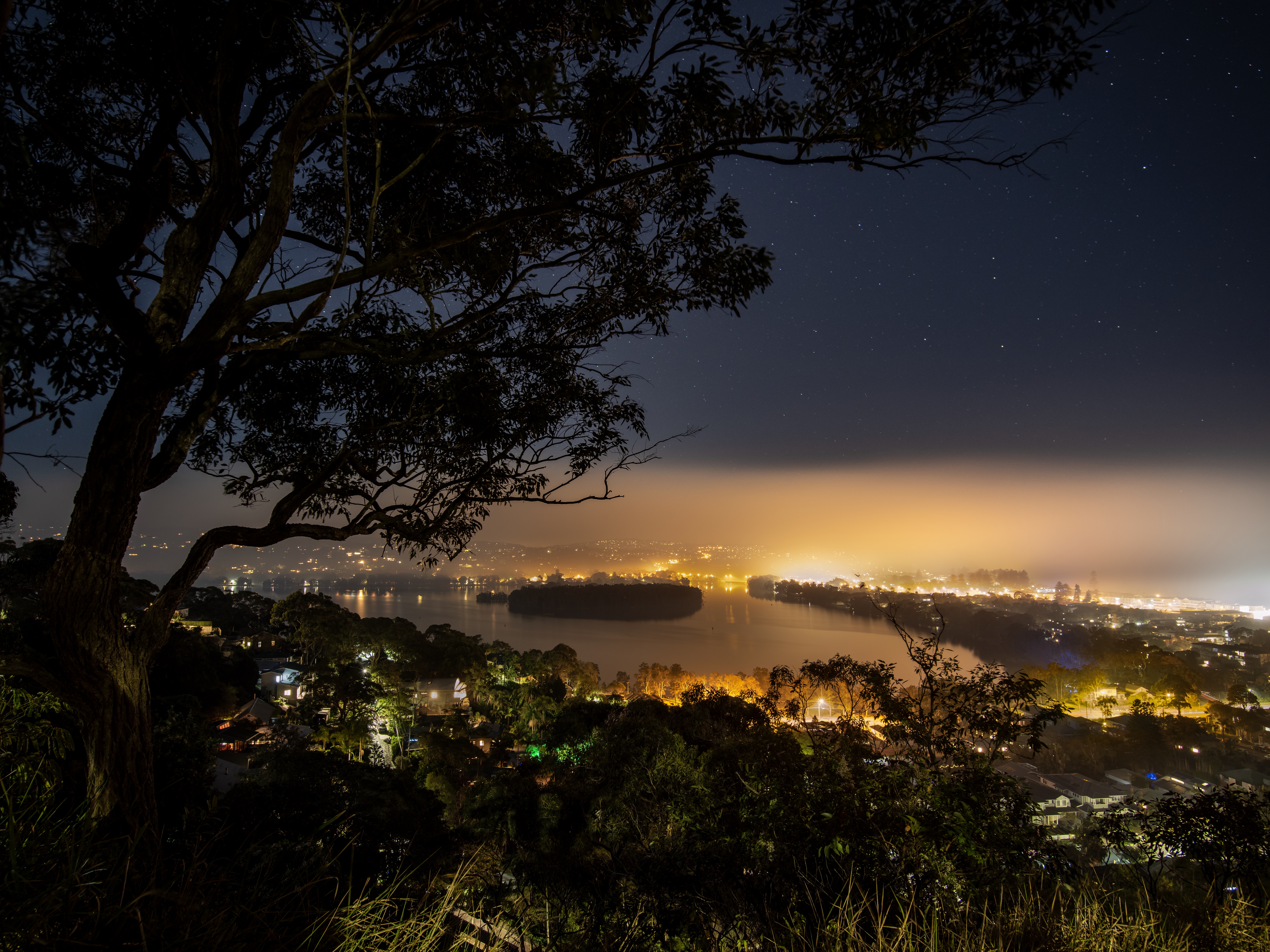 A low-lying haze conceals twinkling stars above Lake Narrabeen and Turimetta Head on Sydney’s Northern Beaches