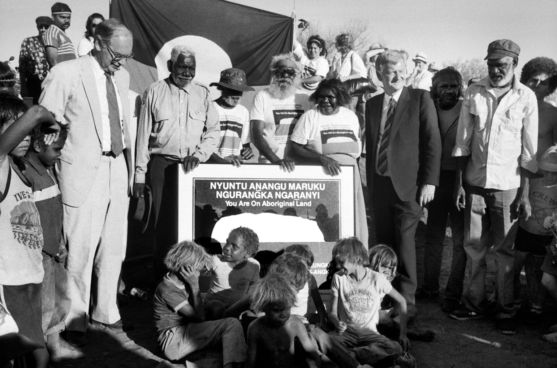 Anangu Traditional Owners Peter Bulla, Peter Kanari, Nipper Winmarti, Barbara Tjirkadu and their families celebrate with Governor-General Sir Ninian Stephen and Labor Minister Barry Cohen at the Uluru handback ceremony on 26 October 1985